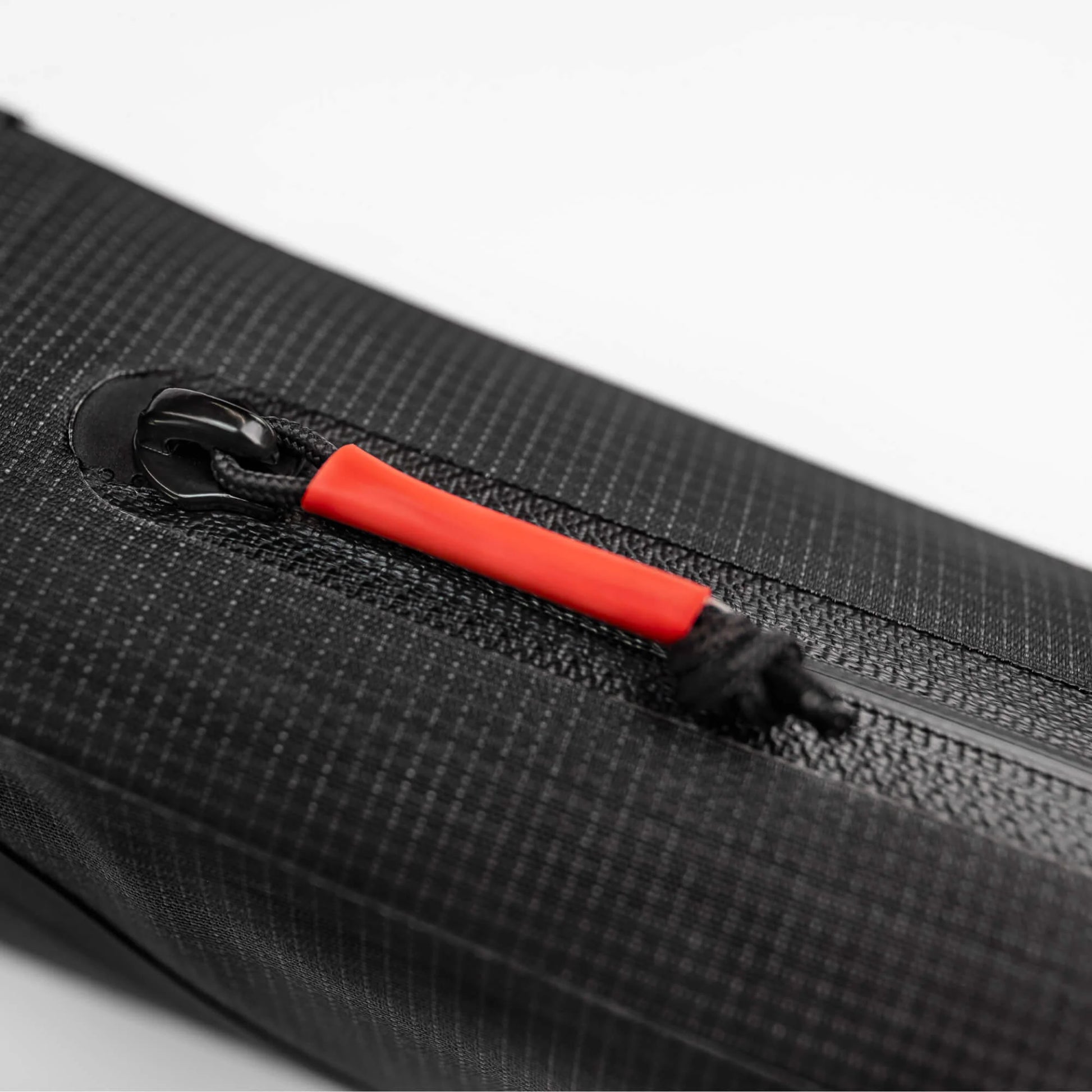 Gros plan sur la fermeture éclair étanche et la tirette rouge de la sacoche top tube noire CYCLITE. (Noir)