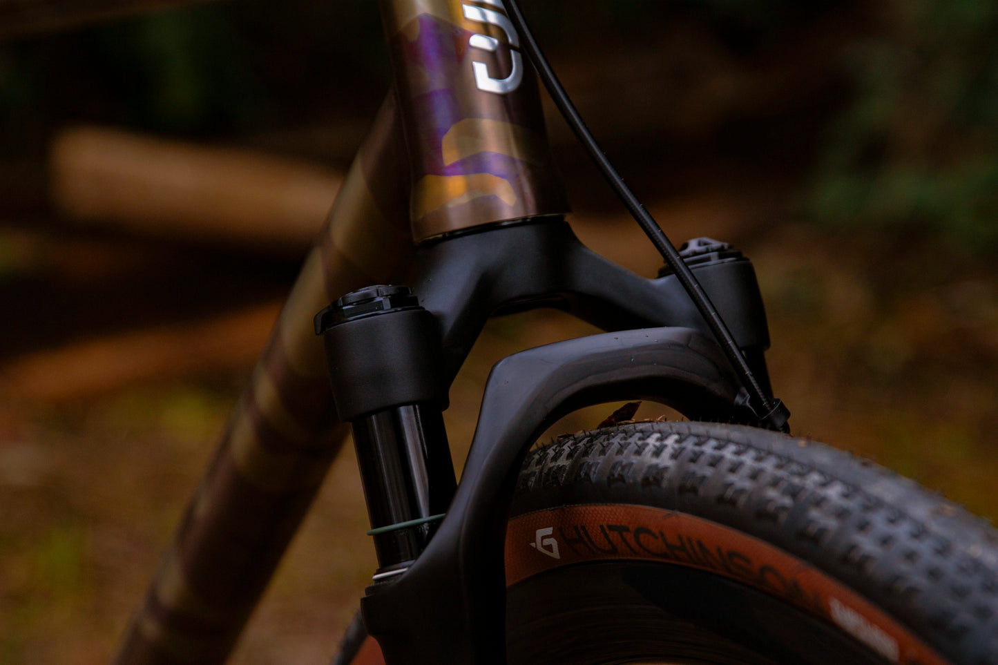 Vue latérale avant d'un vélo complet CYKL GRAAVE. Le cadre en aluminium anodisé violet "camo" avec lettrage GRAAVE est équipé de la fourche suspendue KS GTC de 40mm (arceau carbone visible, plongeurs 30mm). Poste de pilotage gravel, freins Flat Mount et pneu gravel volumineux. Passage externe de la durite de frein.
