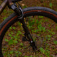 Vue d'ensemble de trois quarts arrière d'un vélo complet CYKL GRAAVE. Cadre aluminium anodisé violet "camo" avec fourche suspendue KS GTC installée à l'avant. Transmission SRAM Force eTap AXS 1x, pédalier SRAM Force Quarq avec capteur de puissance, roues gravel, tige de selle carbone et accessoires validés par CYKL (porte-bidons, sacoche). Visualisation de la géométrie complète.