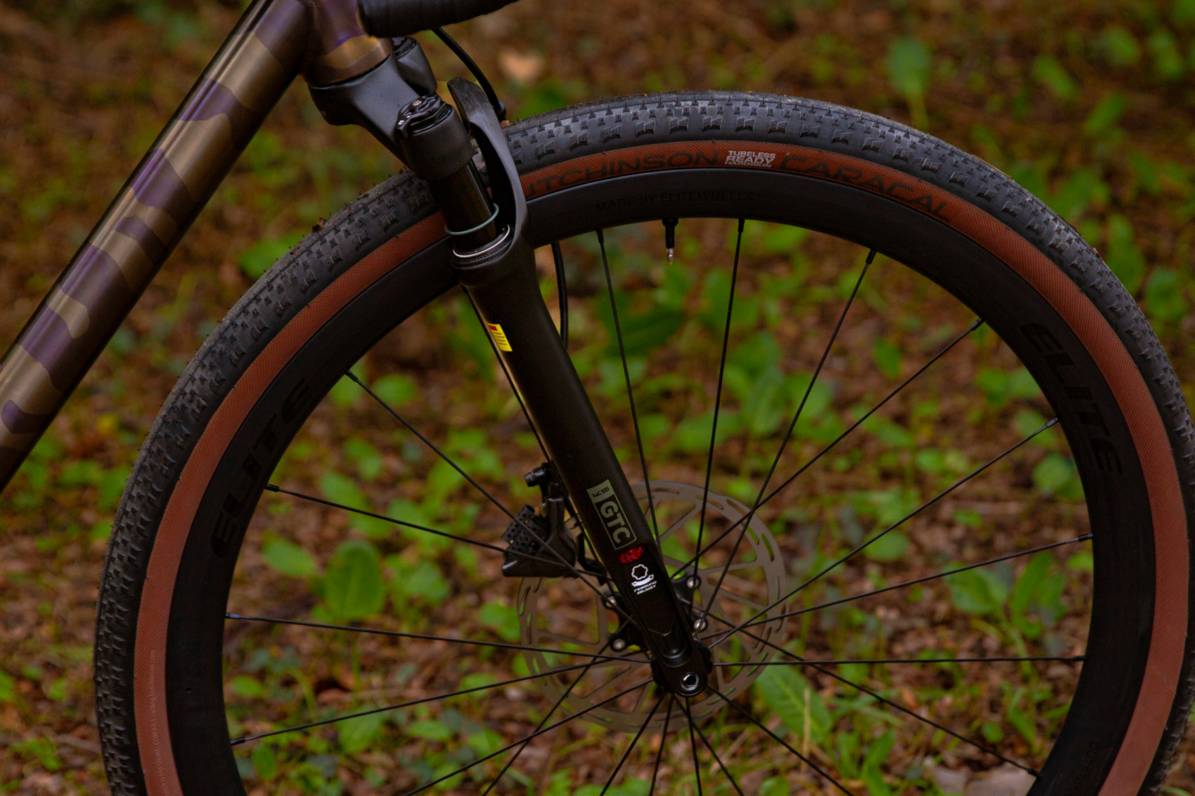 Vue d'ensemble de trois quarts arrière d'un vélo complet CYKL GRAAVE. Cadre aluminium anodisé violet "camo" avec fourche suspendue KS GTC installée à l'avant. Transmission SRAM Force eTap AXS 1x, pédalier SRAM Force Quarq avec capteur de puissance, roues gravel, tige de selle carbone et accessoires validés par CYKL (porte-bidons, sacoche). Visualisation de la géométrie complète.